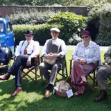 a group of peopple sat in deckchairs dressed in 1940s clothing