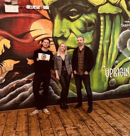 a female and two males dressed in casual clothing against a decorated brick wall