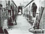 black and white photo of alleyway with old car and various items around