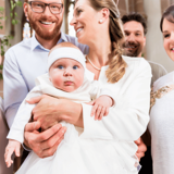 group of adults surrounding baby dressed in white