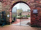 half closed wrought iron gate in red brick arch with garden beyond