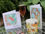 a champagne flute of pink fizz on a garden table with cards, keyrings and a pot