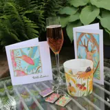 a champagne flute of pink fizz on a garden table with cards, keyrings and a pot