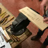 person carving their initials into wood using traditional methods