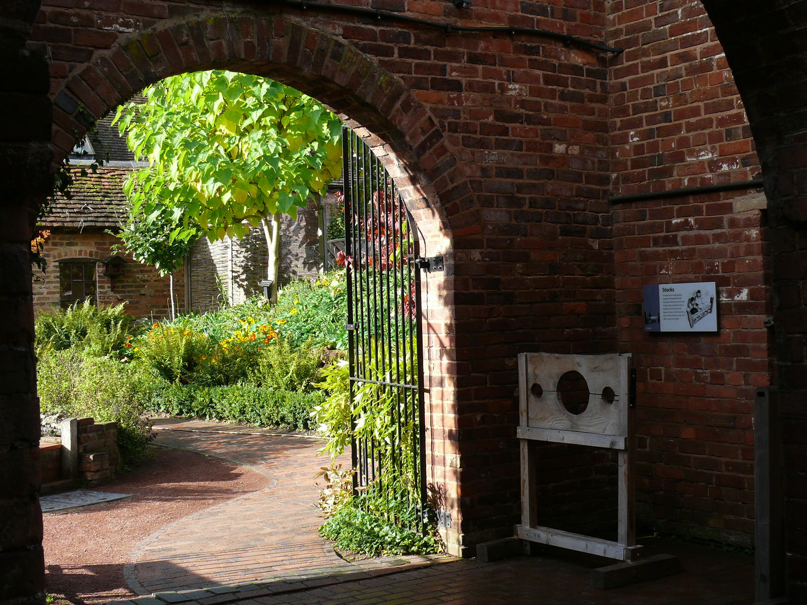 Georgian building gated entrance to gardens with old jail stocks at entrance
