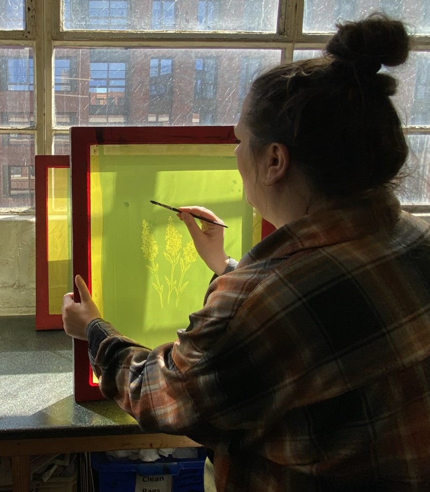 female sat facing window painting on textile