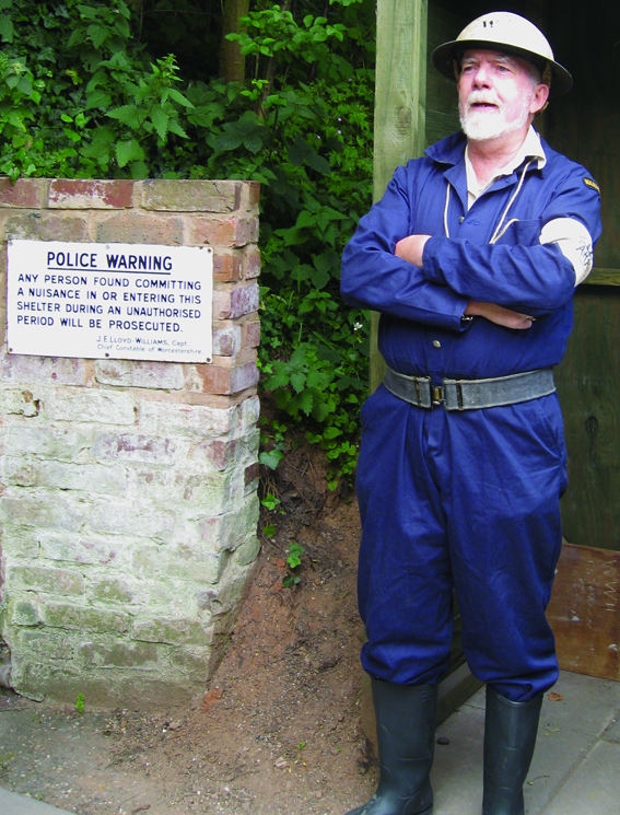 Elderly male wearing World War 2 military police uniform outside an underground air raid shelter